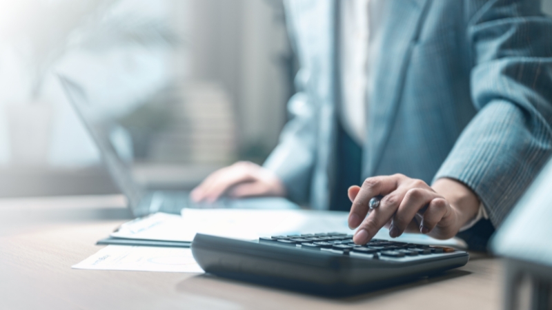 Preduzetnik u kancelariji koristi kalkulator i računar tokom procesa otvaranja poslovnog računa za firmu