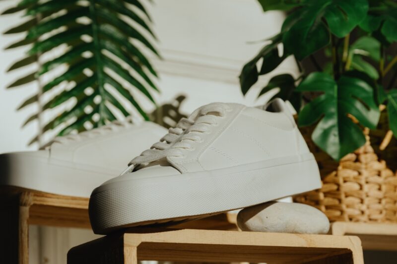 prikaz belih patika na drvenom stolu sa listovima palme pored