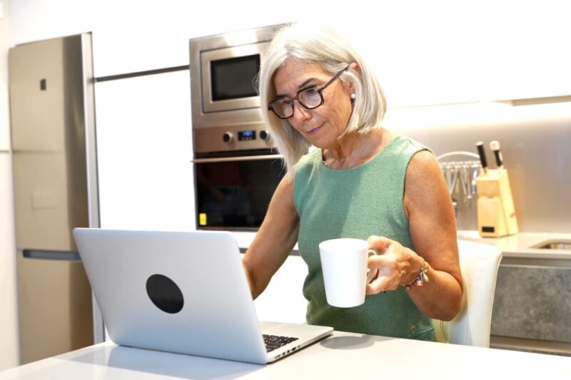 prikaz žene koja koristi laptop i drži kafu u ruci